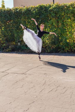 Beyaz etekli kadın balerin altın bir sonbahar parkında sivri ayakkabılarla dans ediyor. Balerin güzel bir bale pozisyonunda duruyor.