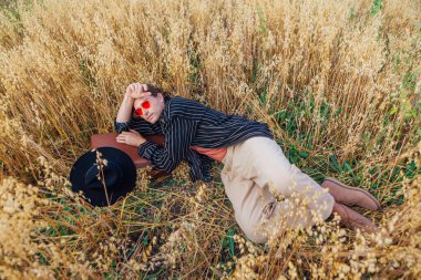 Kırsal Kır Sahnesi. Siyah gömlek ve pembe güneş gözlüğü takmış uzun boylu yakışıklı bir adam altın yulaf tarlasında içi yulaf dolu kahverengi deri valiziyle yatıyordu. Mavi gökyüzü ile yaz manzarası