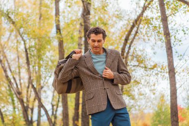 Kahverengi ceketli uzun boylu yakışıklı bir adam sonbahar sokağında çantasıyla yürüyor.