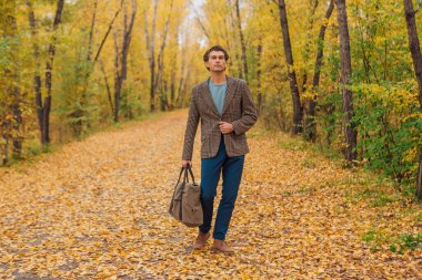 Kahverengi ceketli uzun boylu yakışıklı bir adam sonbahar sokağında çantasıyla yürüyor.