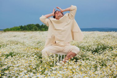 Beyaz takım elbiseli uzun boylu, yakışıklı bir adam papatya çiçekleri tarlasında bir sandalyenin arkasında oturuyordu.