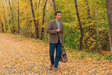 Kahverengi ceketli uzun boylu yakışıklı bir adam sonbahar sokağında çantasıyla yürüyor.