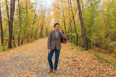 Kahverengi ceketli uzun boylu yakışıklı bir adam sonbahar sokağında çantasıyla yürüyor.