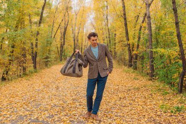 Kahverengi ceketli uzun boylu yakışıklı bir adam sonbahar sokağında çantasıyla yürüyor.