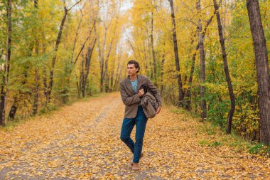 Kahverengi ceketli uzun boylu yakışıklı bir adam sonbahar sokağında çantasıyla yürüyor.
