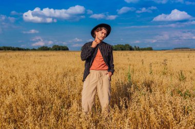 Kırsal Kır Sahnesi. Siyah gömlekli ve siyah şapkalı uzun boylu yakışıklı adam altın yulaf tarlasında duruyordu. Mavi gökyüzü ile yaz manzarası