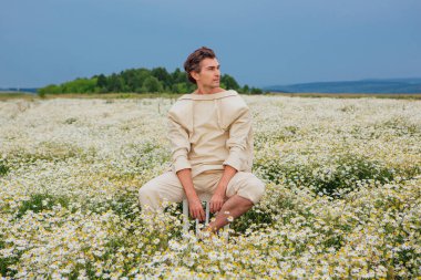 Papatya çiçekleri tarlasında bir sandalyenin arkasında oturan uzun boylu yakışıklı adam.