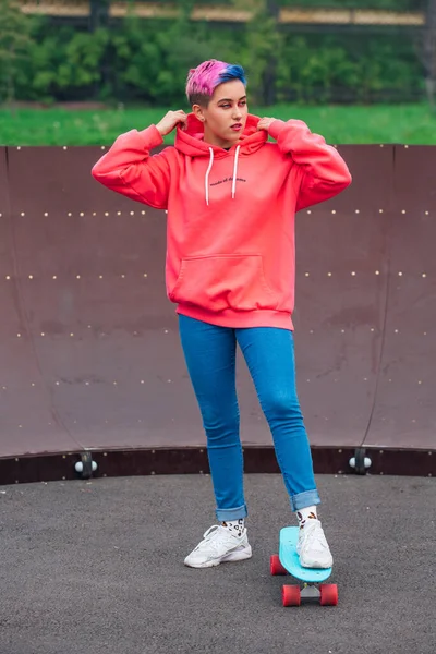 Retrato de una jovencita guapa de moda parada junto a la pista de skate con su monopatín de plástico. —  Fotos de Stock