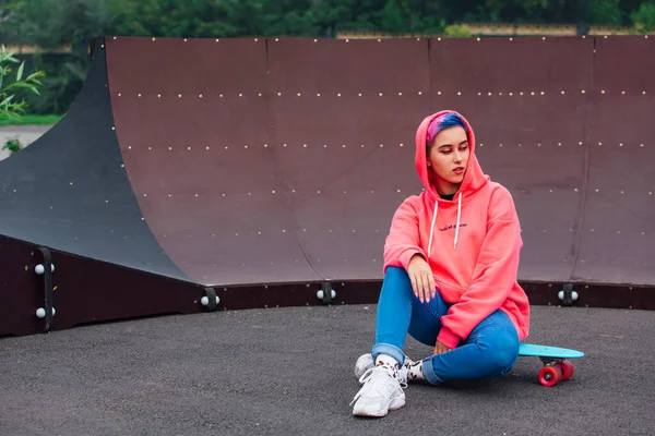 Portret van een trendy mooi jong meisje naast de skateboard court op haar plastic skateboard. — Stockfoto