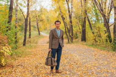 Kahverengi ceketli uzun boylu yakışıklı bir adam sonbahar sokağında çantasıyla yürüyor.