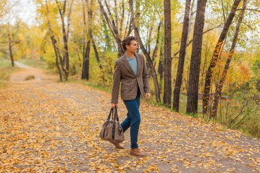 Kahverengi ceketli uzun boylu yakışıklı bir adam sonbahar sokağında çantasıyla yürüyor.
