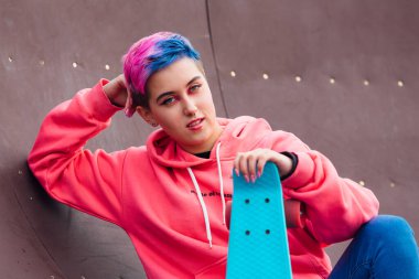 Mavi plastik kaykayıyla parka oturan kısa boylu, şık bir genç kadın. Gençlik kavramı.