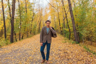 Kahverengi ceketli uzun boylu yakışıklı bir adam sonbahar sokağında çantasıyla yürüyor.