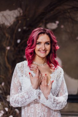 Beton zemin ve duvarları olan karanlık bir odada, yumuşak dantelli bir peignoir giymiş bir kadının portresi.