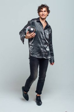 Beyaz arka planda ayna disko topu olan uzun ve çekici bir adamın portresi. Yakışıklı bir adam stüdyoda parlak bir disko topuyla poz veriyor..