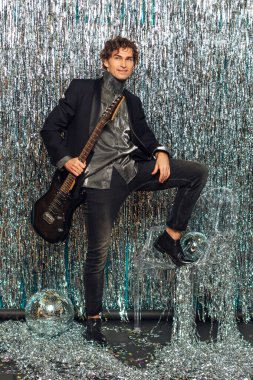 Parlak arka planda elektro gitar tutan uzun boylu çekici bir adam ve yerde ayna disko topu var. Parti konsepti.