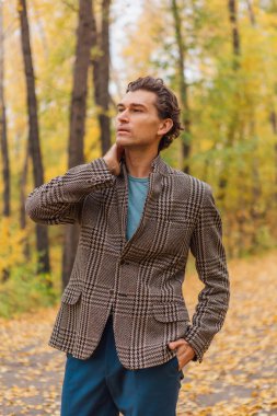 Kahverengi ceketli uzun boylu yakışıklı bir adam sonbahar sokağında yürüyor.