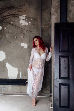 Yumuşak dantelli bir peignoir giymiş kadın beton zemin ve duvarları olan karanlık bir odada çıplak ayakla dikiliyor.