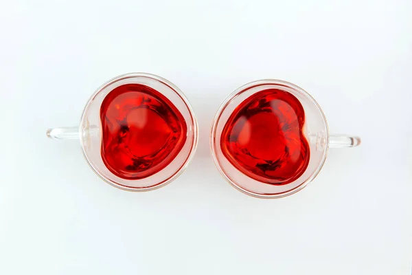 Two transparent heart-shaped cups with tea on the white background. Top view. — Stock Photo, Image