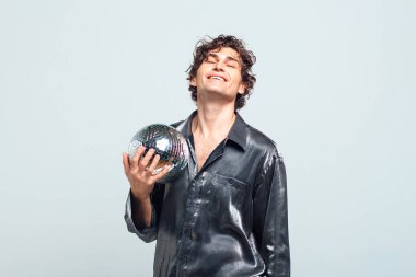 Beyaz arka planda ayna disko topu olan uzun ve çekici bir adamın portresi. Yakışıklı bir adam stüdyoda parlak bir disko topuyla poz veriyor..