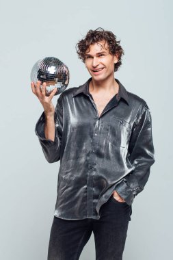 Beyaz arka planda ayna disko topu olan uzun ve çekici bir adamın portresi. Yakışıklı bir adam stüdyoda parlak bir disko topuyla poz veriyor..