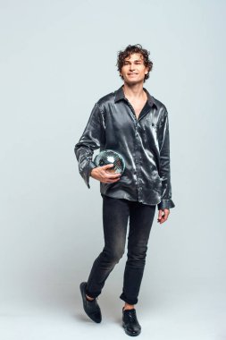 Beyaz arka planda ayna disko topu olan uzun ve çekici bir adamın portresi. Yakışıklı bir adam stüdyoda parlak bir disko topuyla poz veriyor..