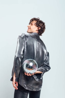 Beyaz arka planda ayna disko topu olan uzun ve çekici bir adamın portresi. Yakışıklı bir adam stüdyoda parlak bir disko topuyla poz veriyor..