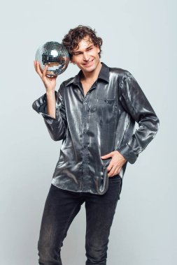 Beyaz arka planda ayna disko topu olan uzun ve çekici bir adamın portresi. Yakışıklı bir adam stüdyoda parlak bir disko topuyla poz veriyor..
