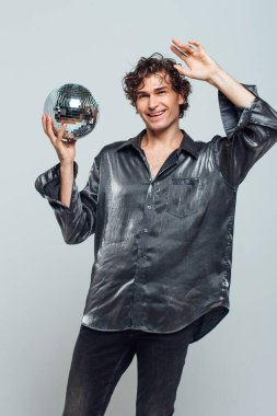 Beyaz arka planda ayna disko topu olan uzun ve çekici bir adamın portresi. Yakışıklı bir adam stüdyoda parlak bir disko topuyla poz veriyor..