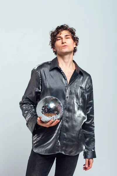 Portrait of tall attractive man with a mirror disco ball on a white background. Handsome man posing with a shiny disco ball in studio.