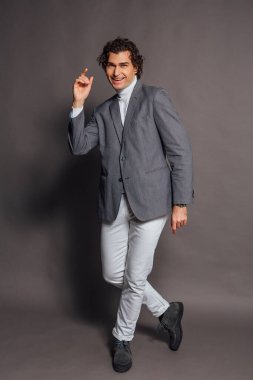 Beyaz balıkçı yaka, beyaz kot pantolon ve gri arka planda poz veren uzun boylu yakışıklı bir adamın moda portresi.