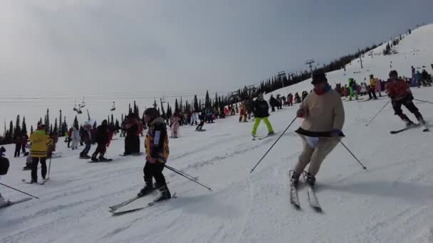 Sheregesh, Kemerovo bölgesi, Rusya - 3 Nisan 2021: Sheregesh Grelka Festivali. Karnaval kostümlü insanlar kar yamacında kayak ve snowboard yapıyor.. — Stok video