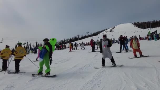 Sheregesh, region Kemerovo, Rusko - 3. dubna 2021: Grelka Fest v Sheregeši. Lidé v karnevalových kostýmech na sněhovém svahu na lyžích a snowboardu. — Stock video