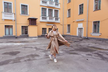 Genç gülümseyen milenyum kadını, yaban saçlarıyla sonbahar paltosu giymiş elinde bir fincan kahveyle eski binanın yakınına gidiyor..