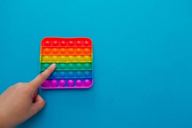 Eller stres önleyici, pop it oyuncağıyla oynar. Gökkuşağı duyusal kıpırdaması mavi arka planda izole edilmiş. Yeni moda silikon oyuncak. Patlayan baloncuk silikon oyuncakları. Boşluğu kopyala.