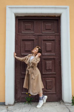 Genç milenyum kadını, eski bir binanın kapısında poz veren, sonbahar paltosu giymiş vahşi saçlı..