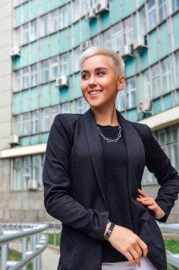 Kısa saçlı ve burnu piercingli şık bir iş kadını. Kendine güvenen kız iş merkezinin yanında duran lezbiyen gibi görünüyor.