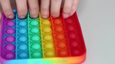 Eller stres önleyici, pop it oyuncağıyla oynar. Gökkuşağı duyusal kıpırdaması beyaz arka planda izole edilmiş. Yeni moda silikon oyuncak. Patlayan baloncuk silikon oyuncakları.