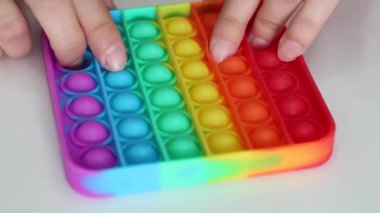 Eller stres önleyici, pop it oyuncağıyla oynar. Gökkuşağı duyusal kıpırdaması beyaz arka planda izole edilmiş. Yeni moda silikon oyuncak. Patlayan baloncuk silikon oyuncakları.