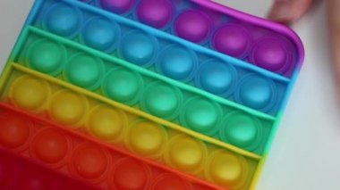 Eller stres önleyici, pop it oyuncağıyla oynar. Gökkuşağı duyusal kıpırdaması beyaz arka planda izole edilmiş. Yeni moda silikon oyuncak. Patlayan baloncuk silikon oyuncakları.