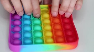 Eller stres önleyici, pop it oyuncağıyla oynar. Gökkuşağı duyusal kıpırdaması beyaz arka planda izole edilmiş. Yeni moda silikon oyuncak. Patlayan baloncuk silikon oyuncakları.