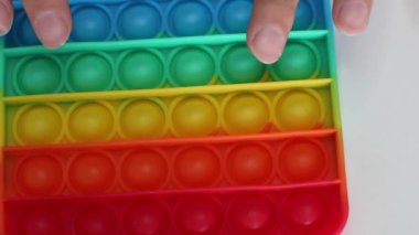 Eller stres önleyici, pop it oyuncağıyla oynar. Gökkuşağı duyusal kıpırdaması beyaz arka planda izole edilmiş. Yeni moda silikon oyuncak. Patlayan baloncuk silikon oyuncakları.