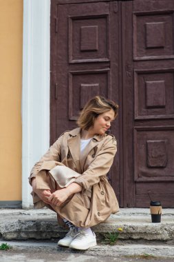 Genç milenyum kadını, sonbahar paltosu giymiş vahşi saçlarıyla eski bir binanın kapısında oturuyor..