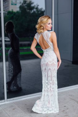 Beyaz gelinlikli güzel sarışın gelin ve açık havada ayna penceresinin yanında duran parlak makyaj..