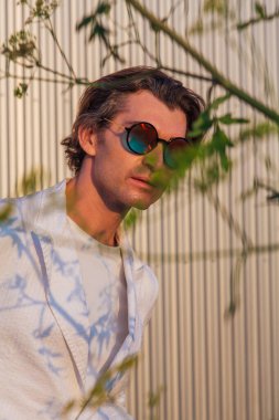 Güneş batarken yuvarlak güneş gözlüklü yakışıklı bir adamın portresi.