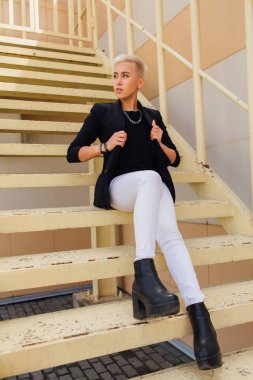 Kısa saçlı ve burnu piercingli şık bir iş kadını. Kendine güvenen kız iş merkezinin yanındaki merdivenlerde oturan lezbiyen gibi görünüyor.