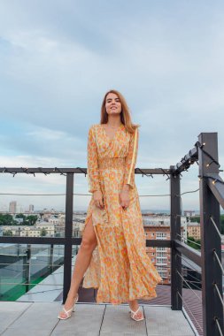 Uzun leopar desenli elbiseli güzel bir kadın bir binanın çatısında merdivenlerde dikiliyor..