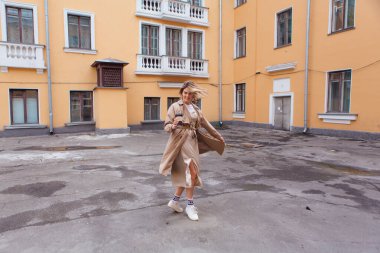 Genç gülümseyen milenyum kadını, yaban saçlarıyla sonbahar paltosu giymiş elinde bir fincan kahveyle eski binanın yakınına gidiyor..