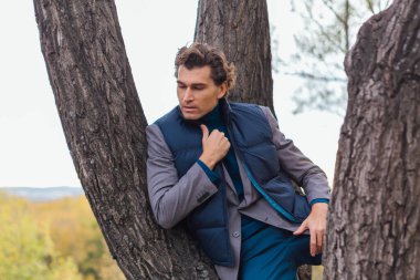 Sarı sonbahar ormanında ağacın yanında duran uzun boylu yakışıklı adam.