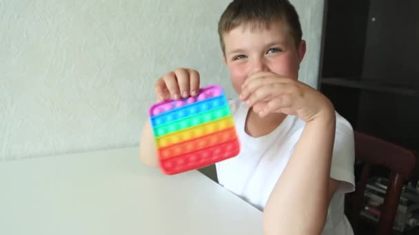 Junge spielt mit Pop it sensorischem Spielzeug. Junge drückt auf bunte regenbogensquishy weiche Silikonblasen. — Stockvideo